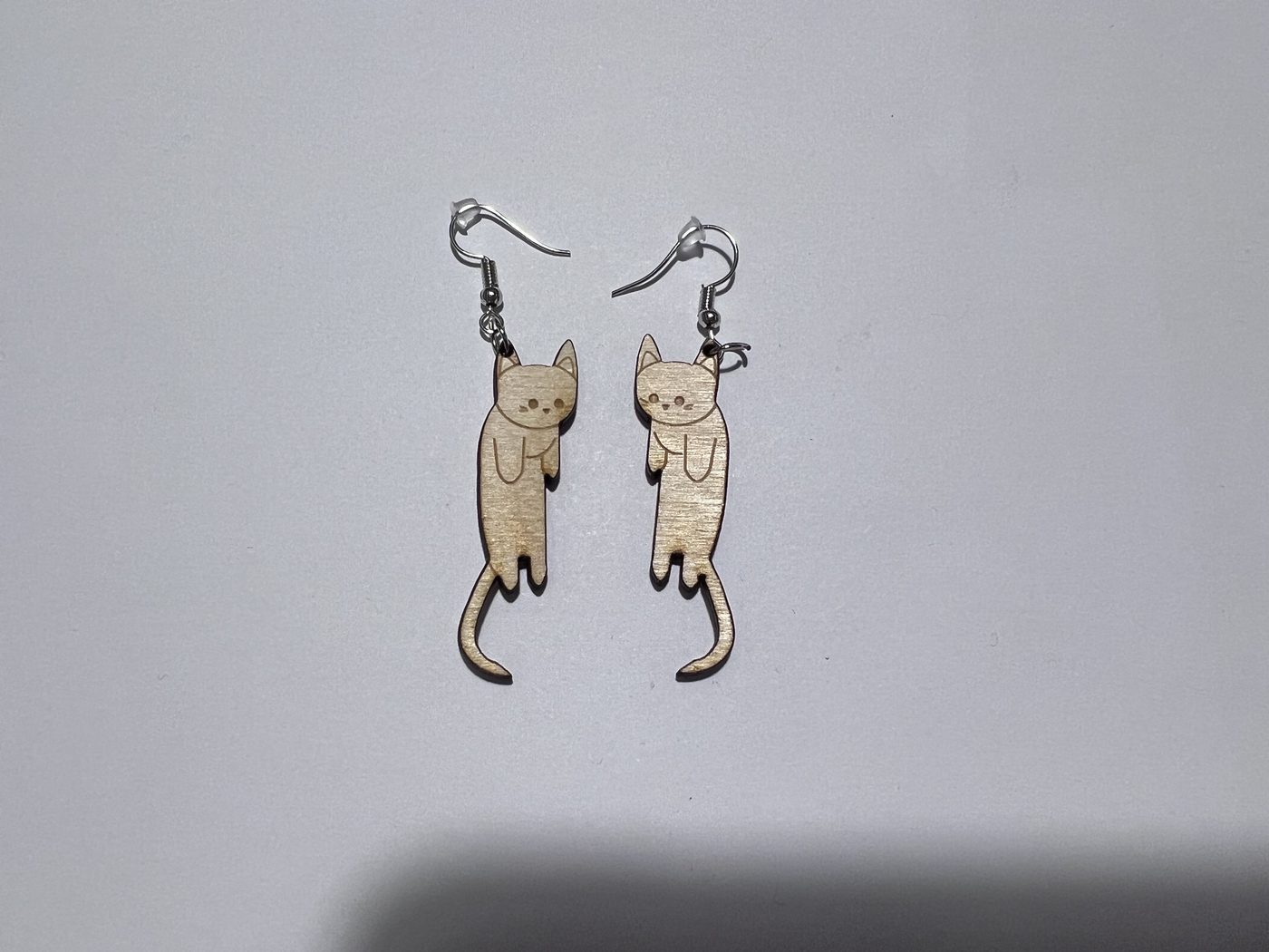 A pair of laser-cut wooden hanging-cat earrings with long curled tails