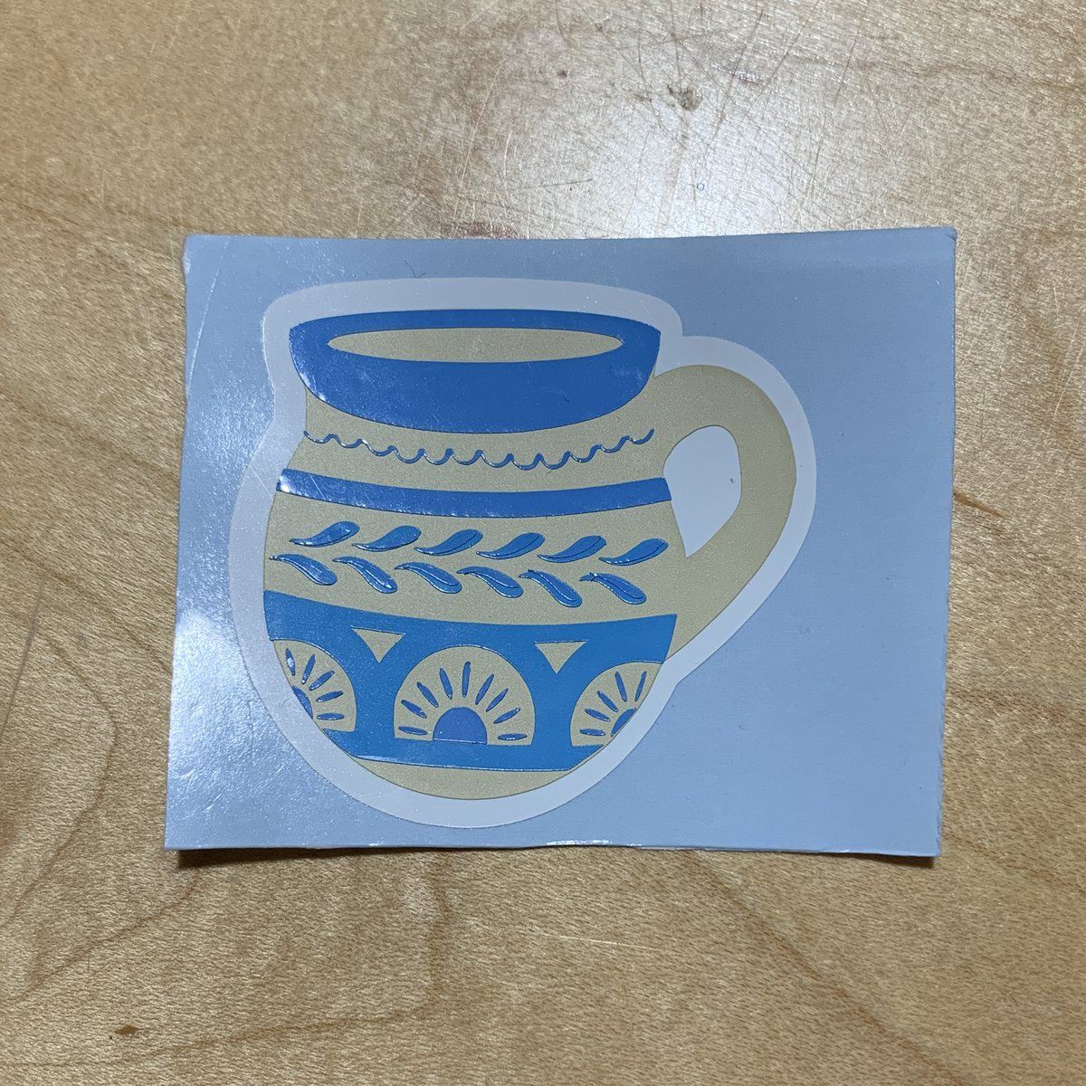 The finished layered vinyl jarrito sticker on its backing sheet, on a wooden table