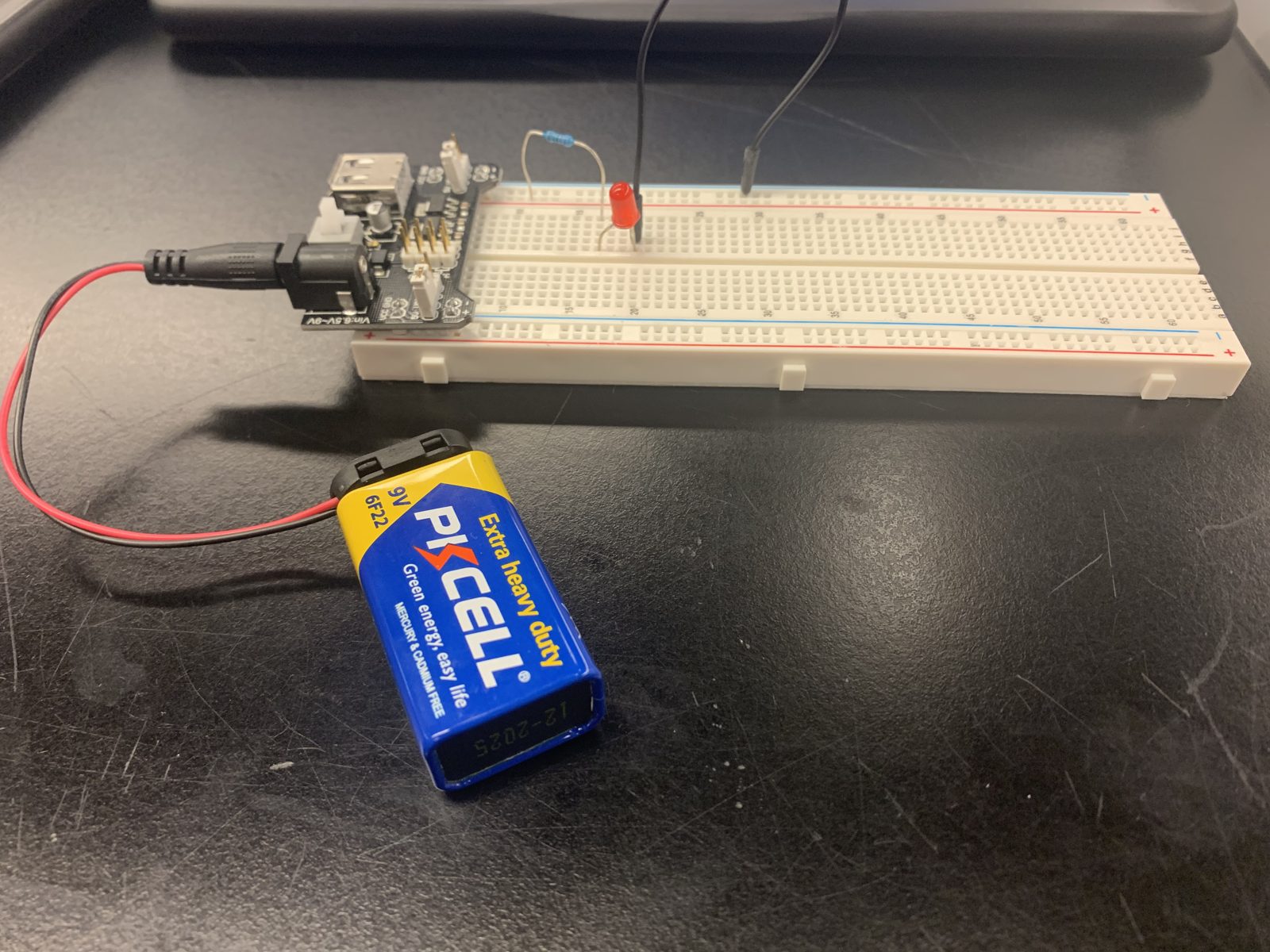 A 9V battery plugged into a breadboard power module, powering a single lit red LED.