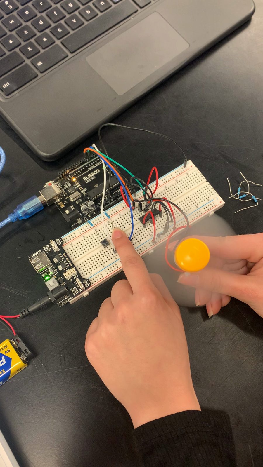 A finger pressing an input on a breadboard while a small DC motor's propeller blurs as it spins.
